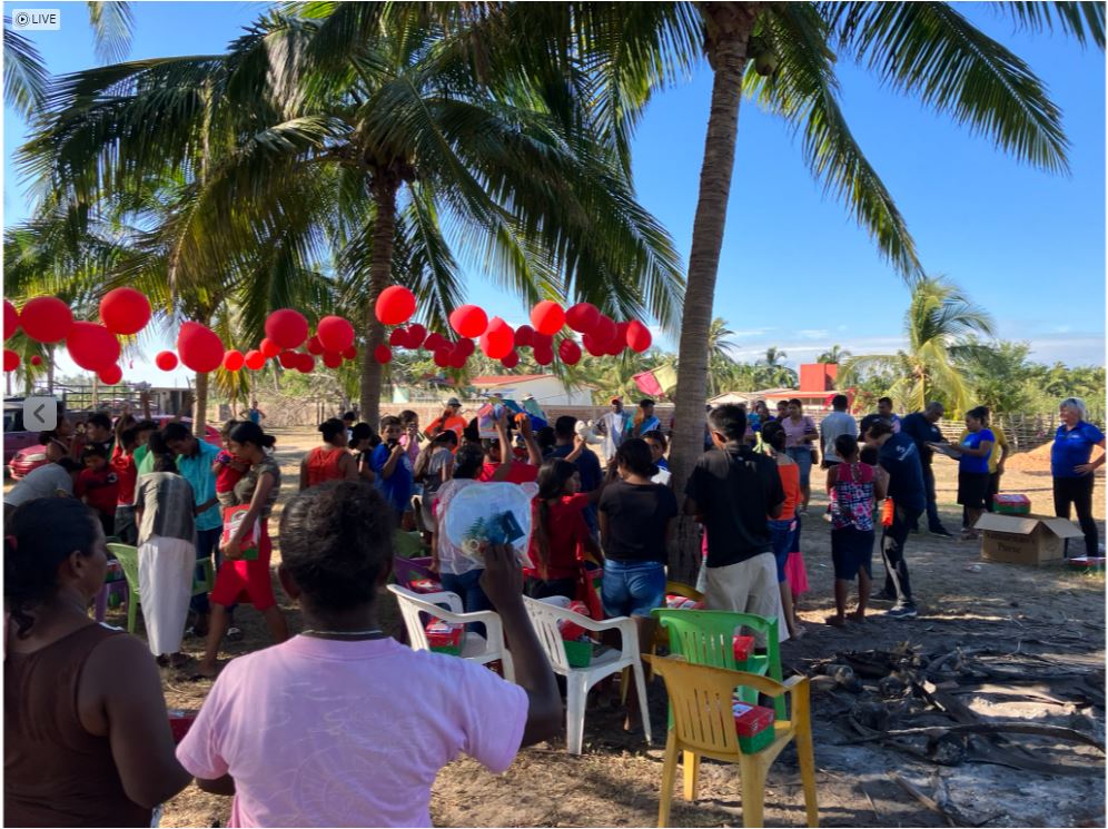 Red balloons among palm trees, many children facing away from camera with adults up front.